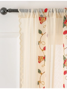 Close-up of Christmas bell embroidery on cream lace curtain with festive light patterns