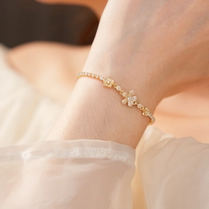 Dettaglio di un bracciale a fiori dorati con zirconi lucenti indossato su un polso