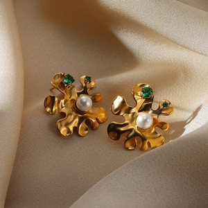 Close-up of gold wavy earrings with white pearl and emerald green stones on silk