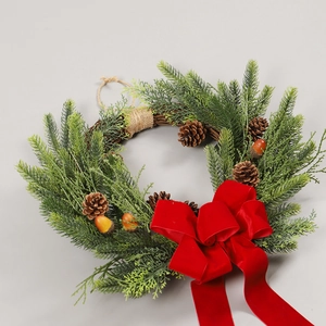 Christmas wreath with green pine needles, cones, and red velvet bow on grey background