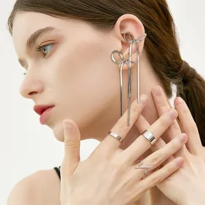 Detailed view of silver bow fringe earrings and geometric rings worn by a model