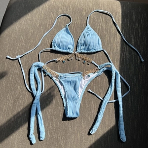 Light blue bikini with gold chains and seashell charms on a textured gray background