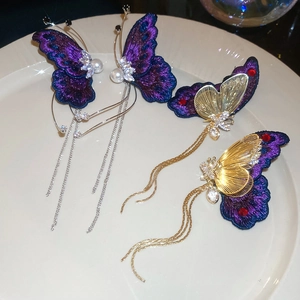 Close-up of embroidered purple butterfly earrings with pearl tassels on a white plate