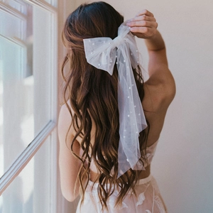 Close-up of a large white tulle bow hair clip with pearls on wavy brown hair