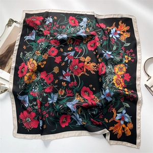 Flat lay of a black floral square silk scarf with red blossoms and beige border edge