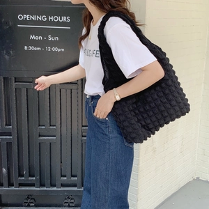 Close-up of black bubble textured tote bag shoulder straps worn on a casual white T-shirt