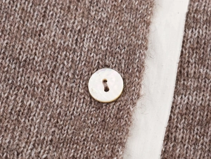 Macro shot of texture of brown knit cardigan with a mother-of-pearl button and white trim
