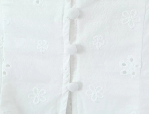 Close-up of white lace embroidery top with delicate floral cutout details and fabric buttons