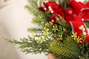 Close-up of red roses, pine needles, and velvet ribbon on a Christmas wreath