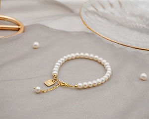 Detailed macro of a freshwater pearl bracelet with golden Good Luck charm on silk