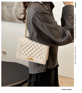 Detail of white quilted crossbody bag featuring a metal rectangular lock and chain strap