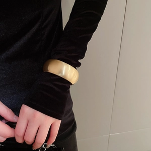 Detail of wide matte gold metal cuff bracelet worn over black velvet sleeve attire