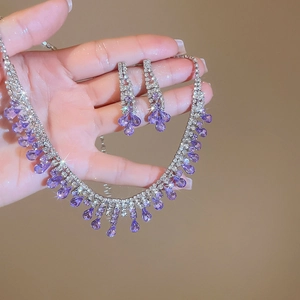 Macro detail of silver tassel necklace and purple teardrop crystal earrings on hand