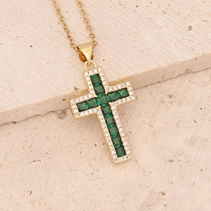 Gold cross necklace featuring green square-cut crystals and clear round zircons on beige stone