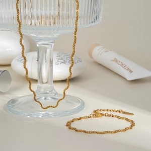 Minimalist gold wave snake chain necklace and bracelet set draped on a glass