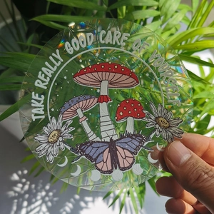 Close-up of holographic mushroom suncatcher sticker held against green foliage