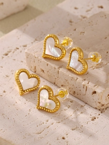 Macro view of heart-shaped earrings with white mother-of-pearl and gold beaded edge detail