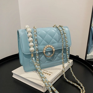 Close-up of light blue quilted chain bag with elegant pearl handle and round pearl clasp