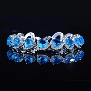 Luxurious heart-shaped sapphire blue tennis bracelet with halo diamonds on black background