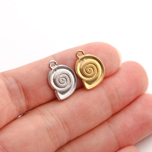 Macro shot of gold and silver spiral shell pendants on a fingertip for size scale