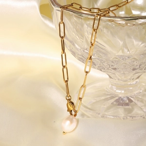 Close-up of gold paperclip chain necklace with a natural pearl pendant on glass