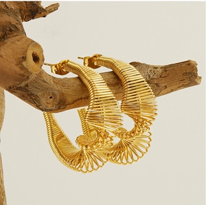 Detail of gold spiral spring earrings hanging on a natural dry branch background