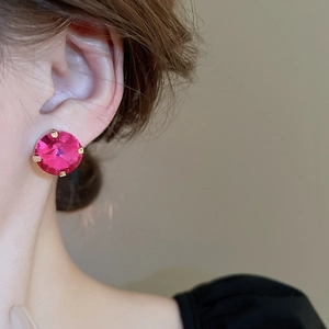 Close-up of a model wearing a gold stud earring with a faceted magenta crystal