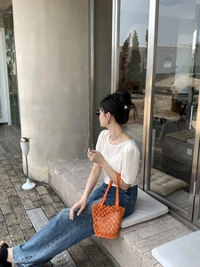 Detailed shot of an orange woven bucket bag styled with white top and denim jeans