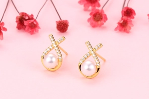 Detail of cross-shaped gold earrings with sparkling zircons and white freshwater pearls
