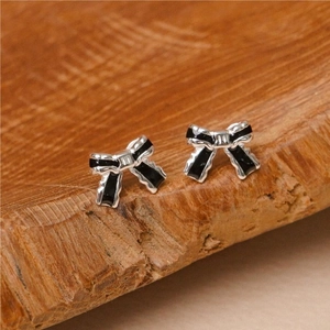 Macro shot of silver bow earrings with black enamel inlay on a wood surface