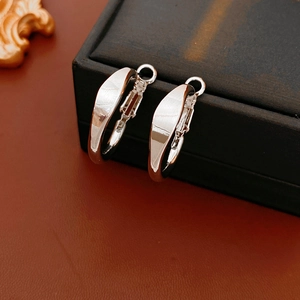 Close-up of polished silver wide hoop earrings on a black textured jewelry box
