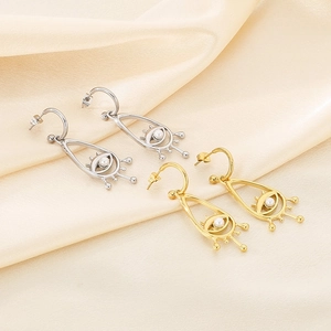Detailed close-up of hollow teardrop earrings with shell evil eye on silk background