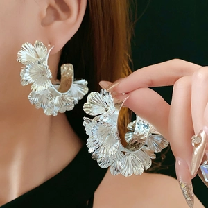 Macro detail of large silver sculpted flower earrings with metallic petals on model