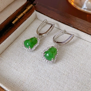 Detailed view of silver gourd earrings with green stones and zircon inlay on a jewelry box