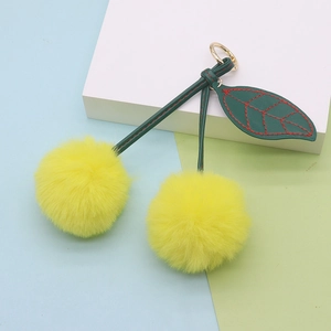 Detailed shot of yellow plush cherry keychain with green leather leaf and gold metal ring