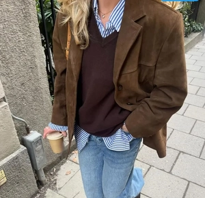 Street style shot of a vintage brown suede jacket with layered knitwear and denim jeans