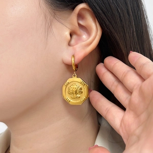 Detailed close-up of a gold octagonal earring featuring an embossed tree motif