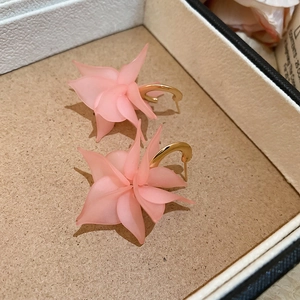 Macro shot of pink acrylic flower earrings with golden hooks on a beige jewelry plate