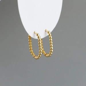 Detailed macro view of gold-plated beaded U-shaped hoop earrings on a white stand