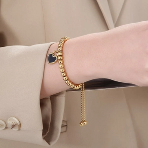 Détail d'un bracelet à perles dorées avec un charme de cœur noir et chaîne réglable