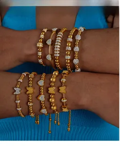 Détail de bracelets dorés avec cœurs, papillons et zircons portés au poignet féminin