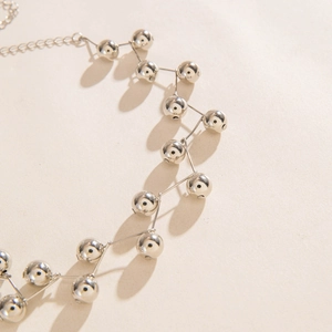 Close-up of silver beaded chain necklace with metallic spheres on textured paper
