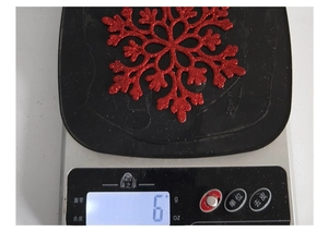 Detail view of 10cm red glitter snowflake decoration being weighed on a scale