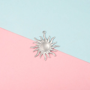 Detailed view of a shiny silver sun charm pendant with wavy rays on a split background