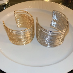 Detailed top view of layered gold and silver open arm cuffs on a white ceramic plate