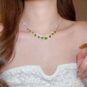 Close-up of elegant silver necklace with green gemstones and tassels on a model's neck