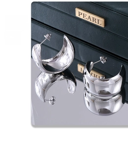 Detailed view of wide high-polished silver C-shaped earrings on mirror with jewelry box