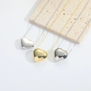 Three minimalist heart pendants in gold, silver and black on a textured stone surface