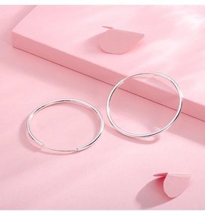 Macro shot of minimalist S999 sterling silver hoop earrings on a soft pink background