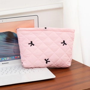Detail of pink quilted cosmetic bag with black embroidered bows on a desk